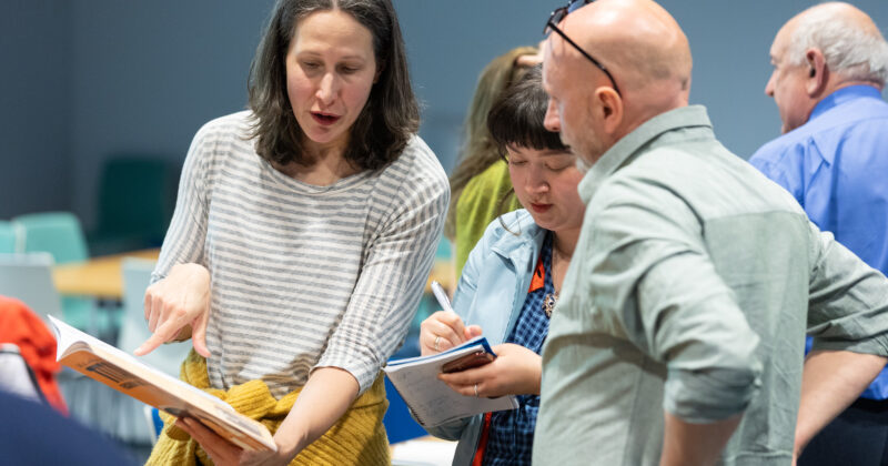 Two woman and one man standing in a small group looking at book.