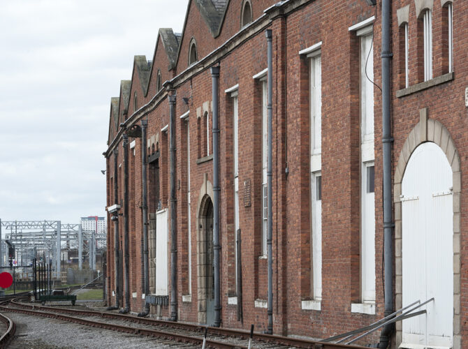 The warehouse stretches along the line with its distinctive sawtooth roof and evenly spaced openings designed for efficient goods handling.
