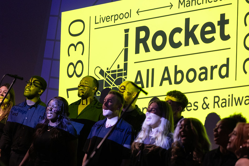 An image of mainly young people singing in front of a Rocket logo