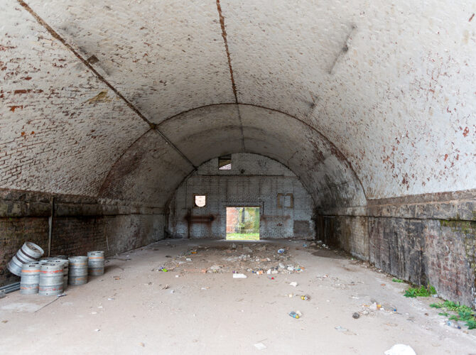 Interior of a spacious arched chamber with a whitewashed brick ceiling, scattered debris on the floor, and small openings at the far end.