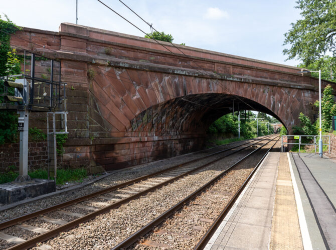 Bright view of the sandstone bridge and adjacent platform, with overhead wires and clear skies.