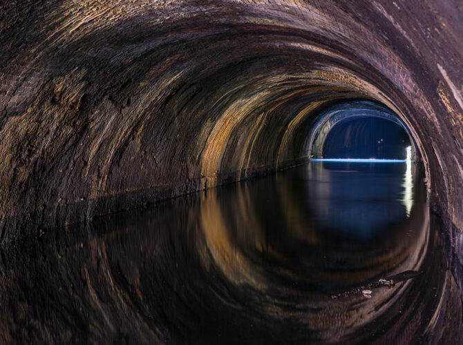 Angled view along the Wapping Tunnel, highlighting the curved brickwork and water pooled along the former track bed.