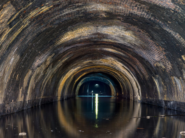 Inside the Wapping Tunnel near Crown Street, showing the brick-lined arch reflected in still water with a faint light in the distance.