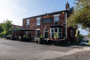 The red-brick Queens Arms building with outdoor seating, canopy and the pub sign above the entrance