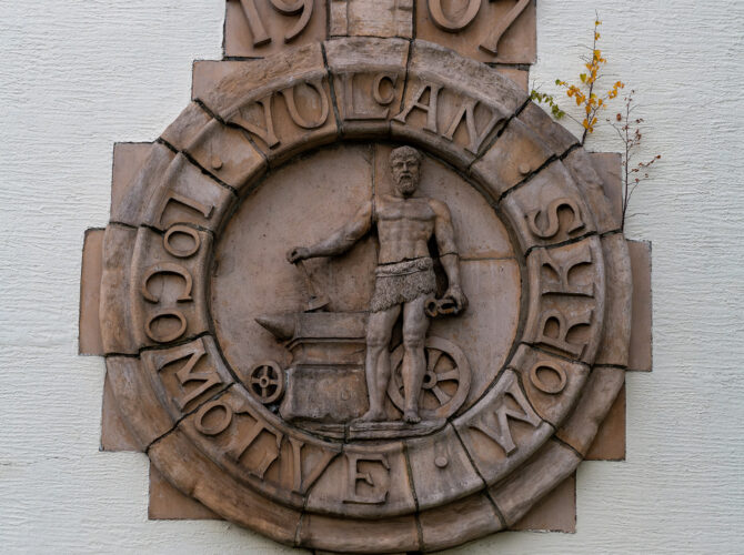 A decorative crest featuring Vulcan, the Roman god of fire and metalworking, commemorates the Vulcan Foundry and its industrial heritage