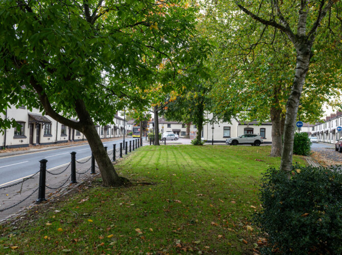 A small village green shaded by mature trees sits between rows of workers’ cottages in Vulcan Village