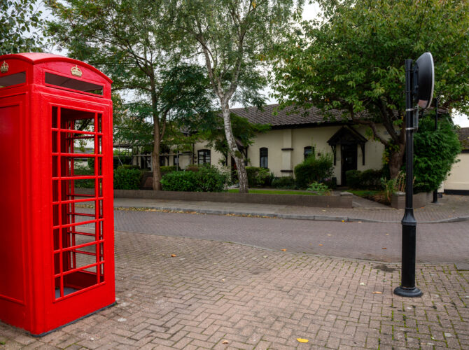 Traditional red telephone box standing near the village green and houses.