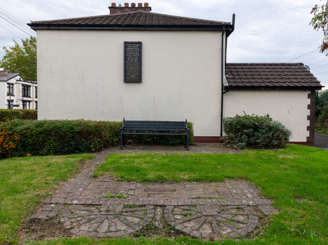 View of a bench and the historic 1835 notice plaque mounted on a house wall.