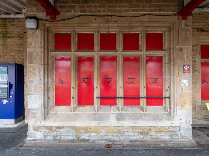 A row of old station windows now filled with red panels featuring small locomotive and wagon designs
