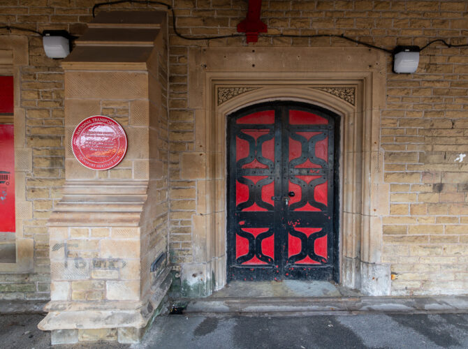 Black and red double doors set within a carved sandstone surround on the platform side of the historic station building.