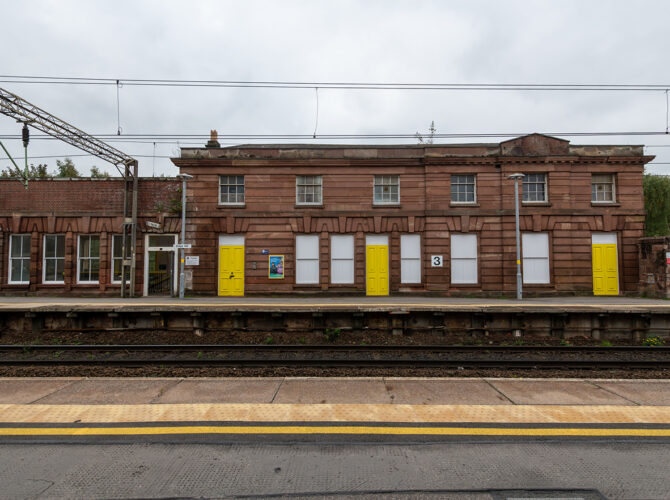 Side view of the station’s long sandstone elevation, featuring symmetrical windows and distinctive yellow-painted doors along the platform.