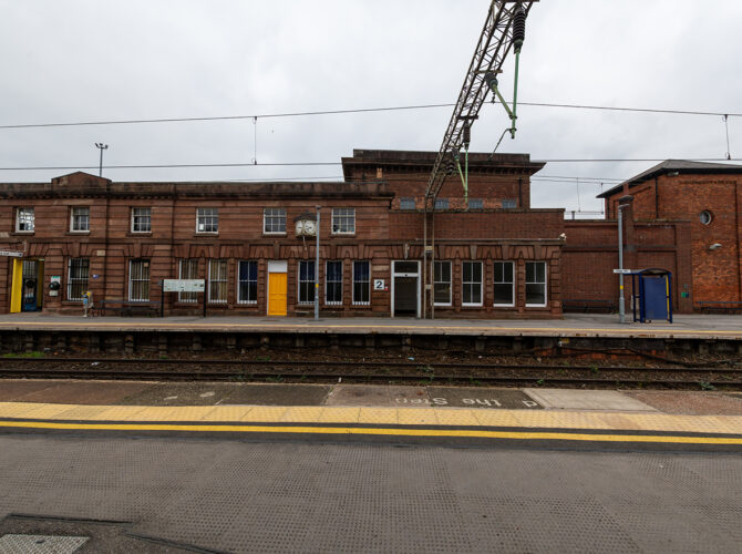 Wide view across the tracks to the sandstone station buildings at Edge Hill, with classical detailing and platform features still in use today.