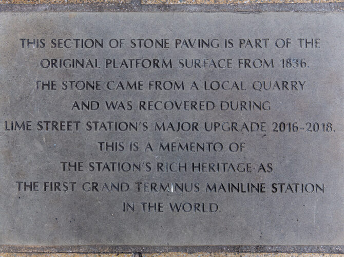 Close-up of a stone plaque explaining that part of the platform paving dates from 1836 and commemorates the station’s historic significance.