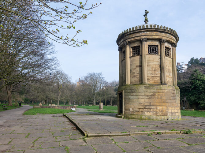 A round stone monument with columns stands in an open paved area of the cemetery.