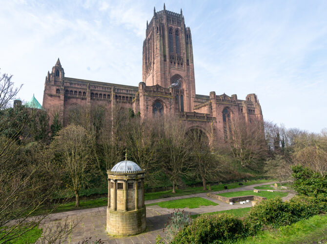 A wider view shows the monument set within paths and greenery, with the Liverpool cathedral above.
