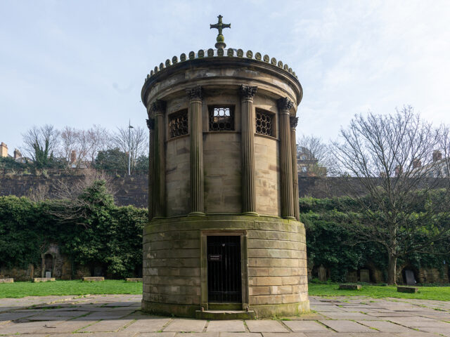 The circular structure features columns and a small gated entrance at ground level.