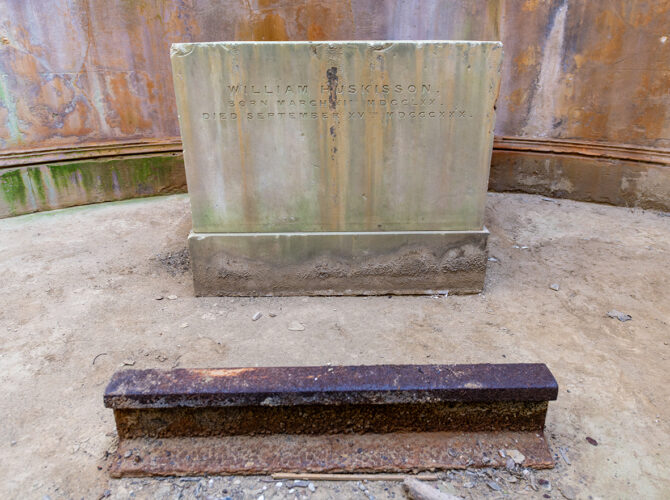 A worn stone inscription sits inside the monument, with a short section of rail placed in front.