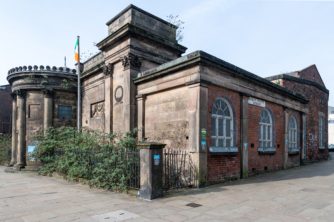 The building’s stone frontage meets a later red-brick section, with arched windows along the side street.
