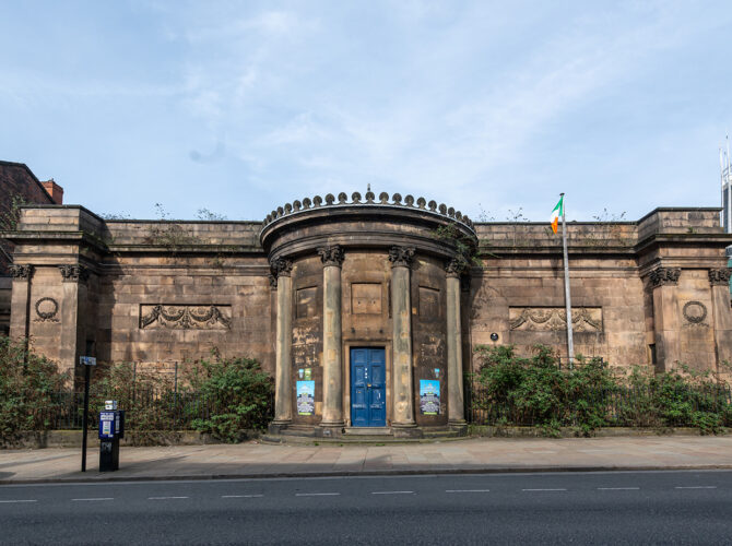A symmetrical façade with a curved portico, columns and a central blue door facing the road.