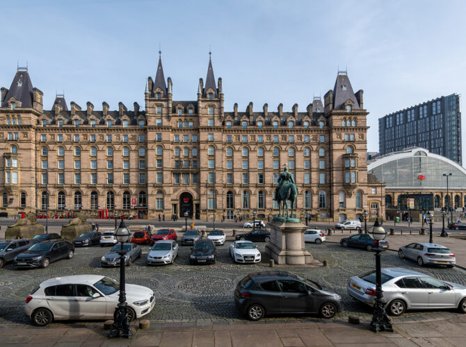 The hotel stands beside Lime Street Station, with an equestrian statue and busy forecourt in front.