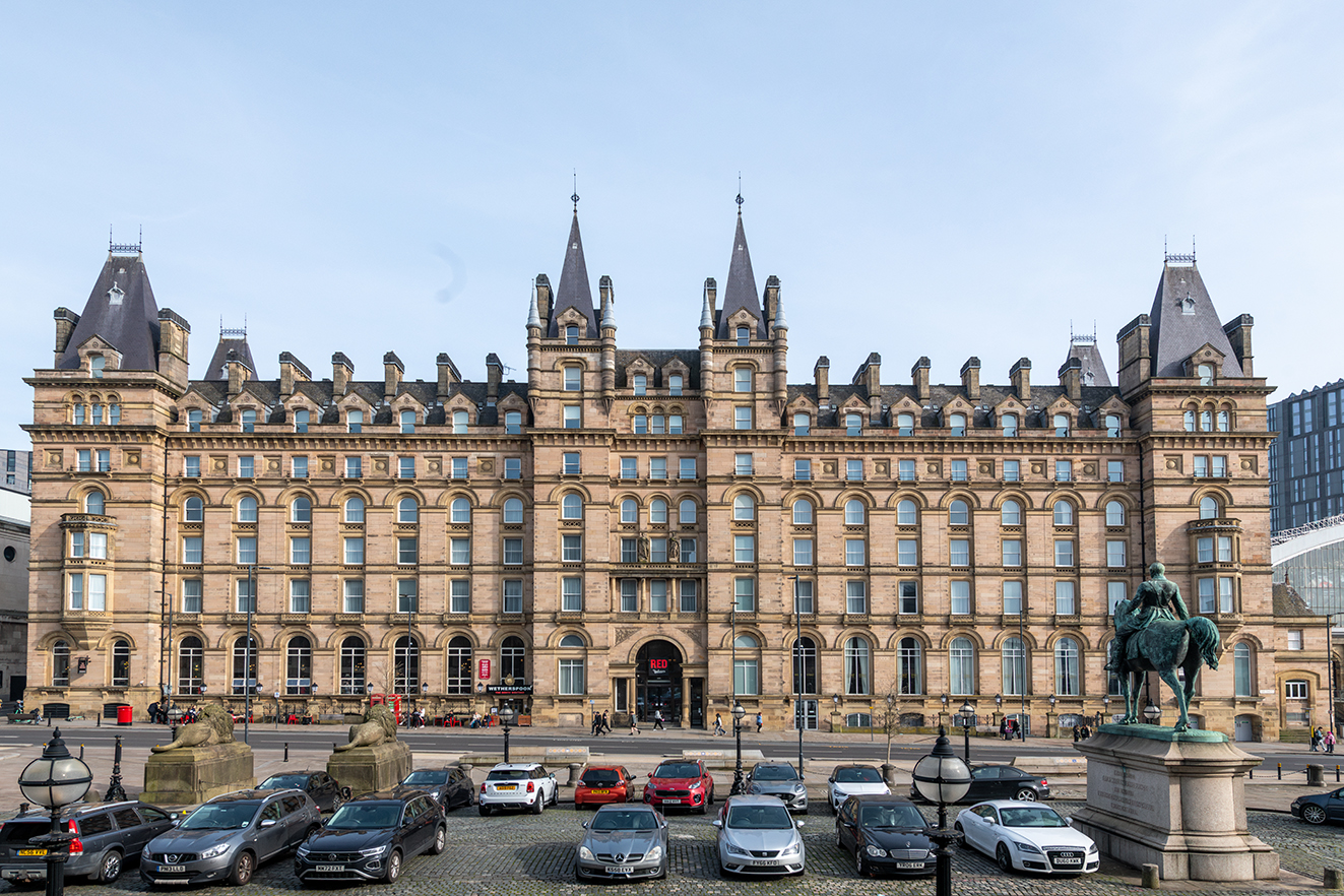 The grand stone façade of the North Western Hotel fills the frame, with parked cars and historic statues in front.