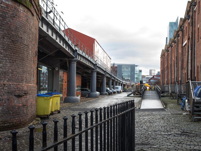 View along a cobbled service road beside the goods depot, showing a brick viaduct carried on a series of arches and columns, with railway structures extending overhead.