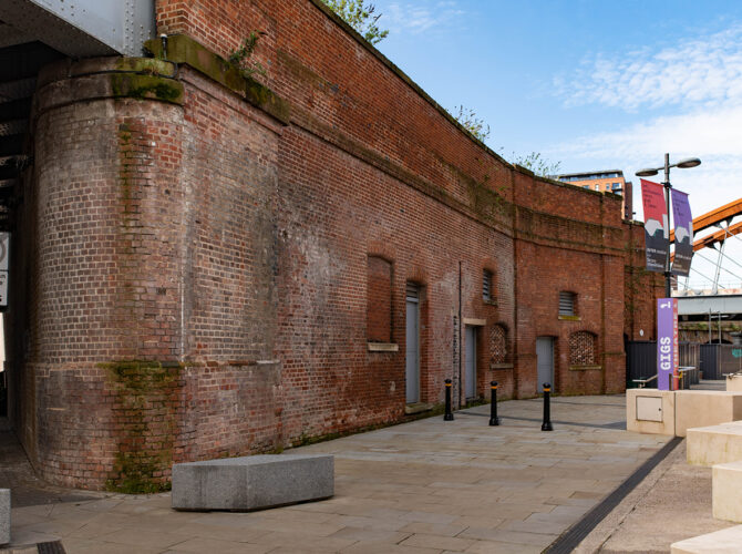 Long section of the former arrivals station showing sealed openings and adapted doorways along a paved area.