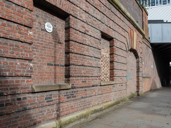 Description: Detailed view of blocked archways and brickwork, with a plaque marking the site’s railway history.