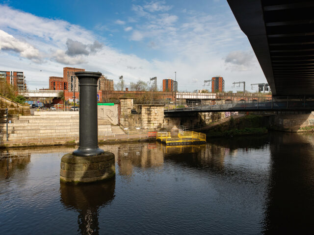 Stone base and iron column stand in the river marking the line of the viaduct towards the warehouse.