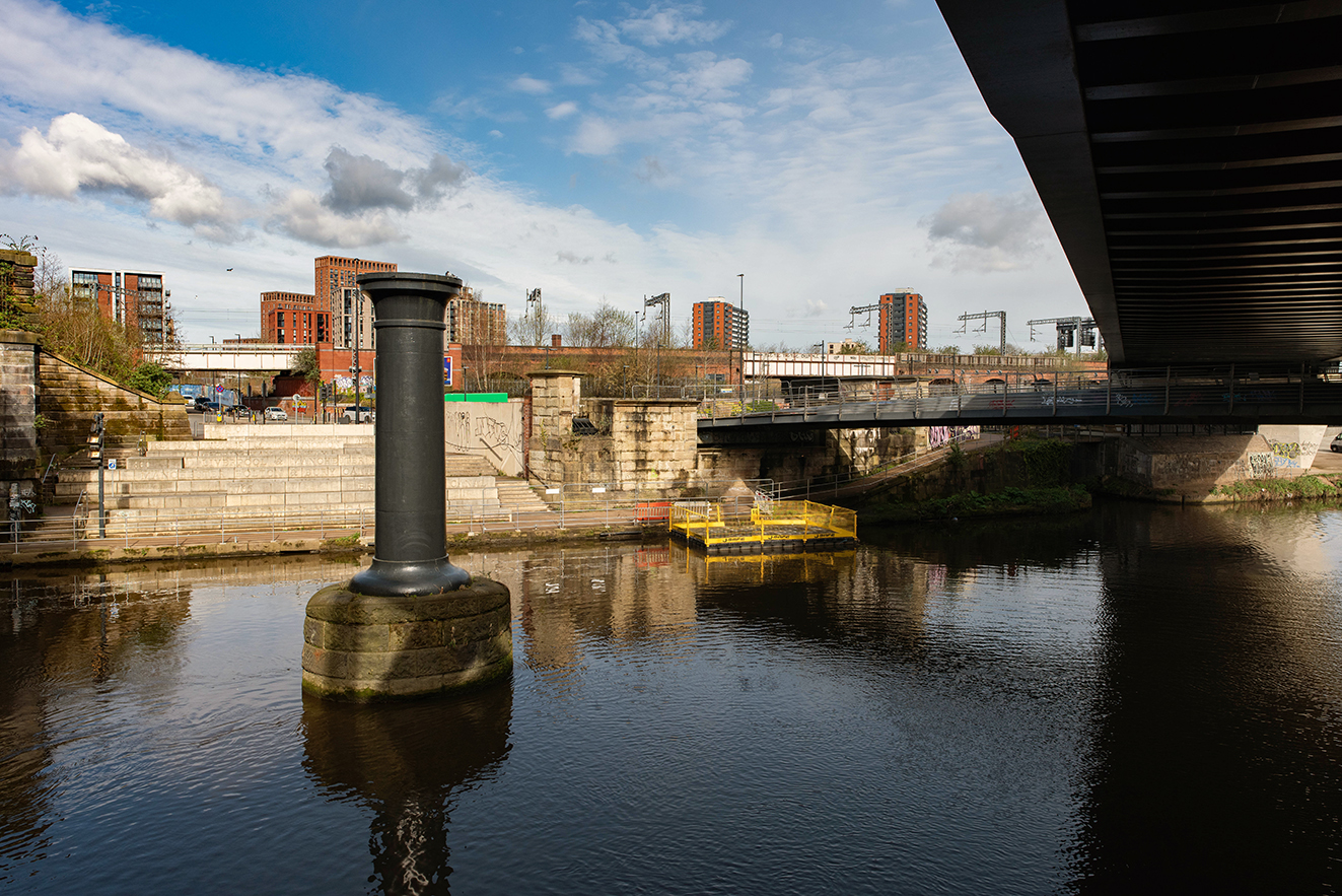 Stone base and iron column stand in the river marking the line of the viaduct towards the warehouse.