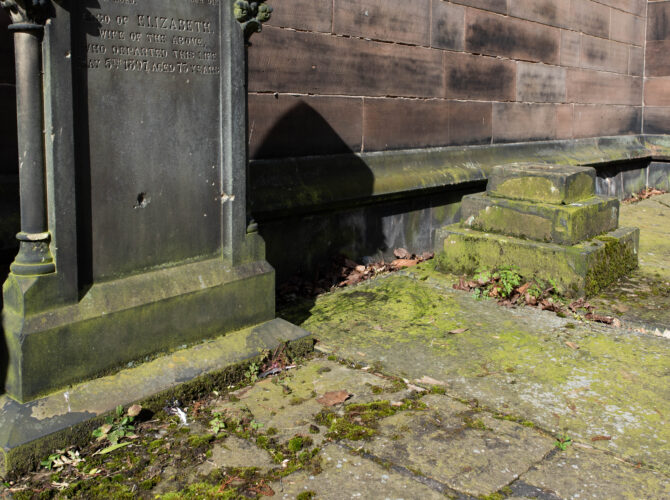 Memorial structure and worn stonework at Stephenson’s grave, set against the church exterior.