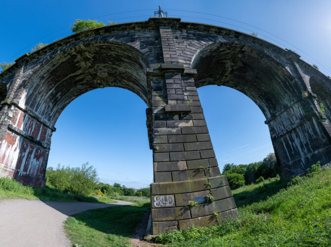 A dramatic low-angle view beneath the viaduct highlighting the massive stone pier and sweeping arches.