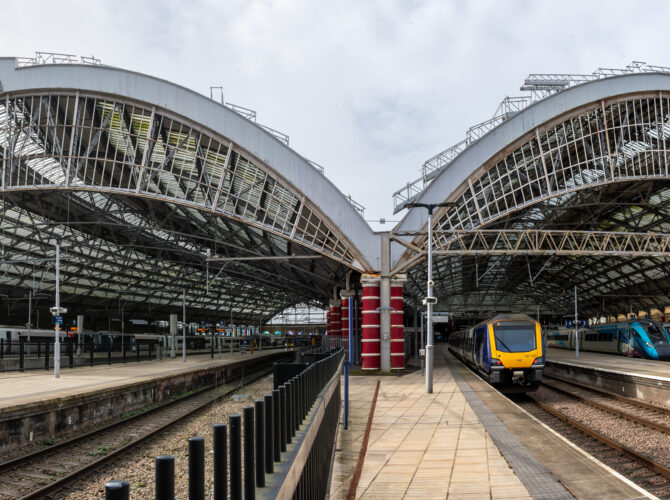 Wide view inside Liverpool Lime Street Station showing two large arched glass-and-iron roofs spanning multiple platforms, with trains on either side and tracks leading into the station.