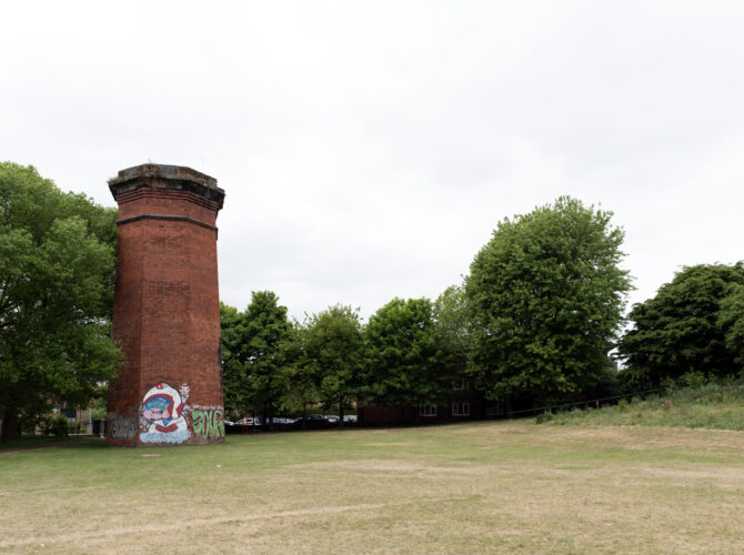 The tall brick Crown Street ventilation tower standing in an open grassy area.