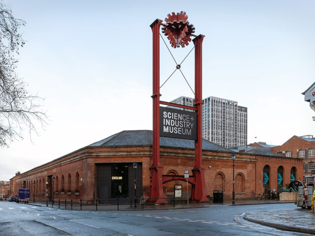 Corner view of the Power Hall with a tall red iron gantry structure marking the museum entrance and surrounding historic buildings.