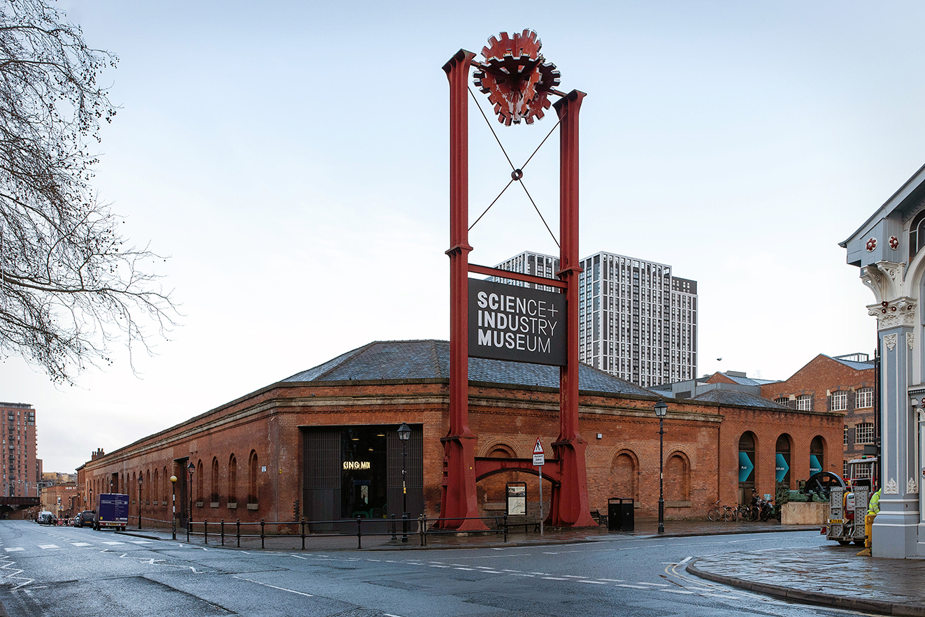 Corner view of the Power Hall with a tall red iron gantry structure marking the museum entrance and surrounding historic buildings.