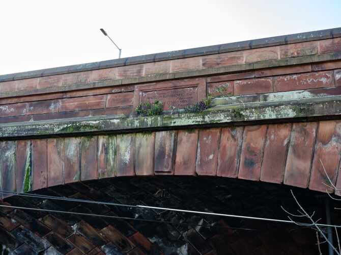 Close-up of an engraved plaque set into the bridge structure, partially weathered.