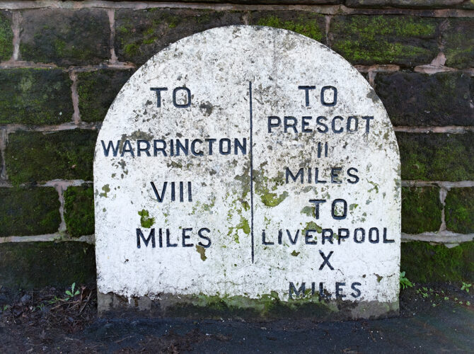 Close-up the weathered milestone indicating distances to Warrington and Liverpool in miles.