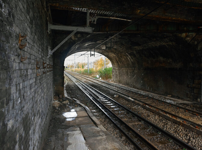 View from beneath the brick railway bridge at Eccles showing the twin tracks passing through the dark arch into open light beyond.
