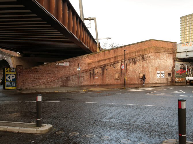 View of a steel railway bridge crossing Water Street, with a sloping brick cattle ramp built into the wall beneath.
