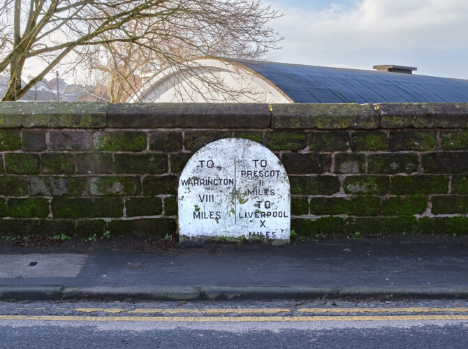 Wider view of a milestone embedded in a wall, indicating distances along the Liverpool and Manchester Railway.