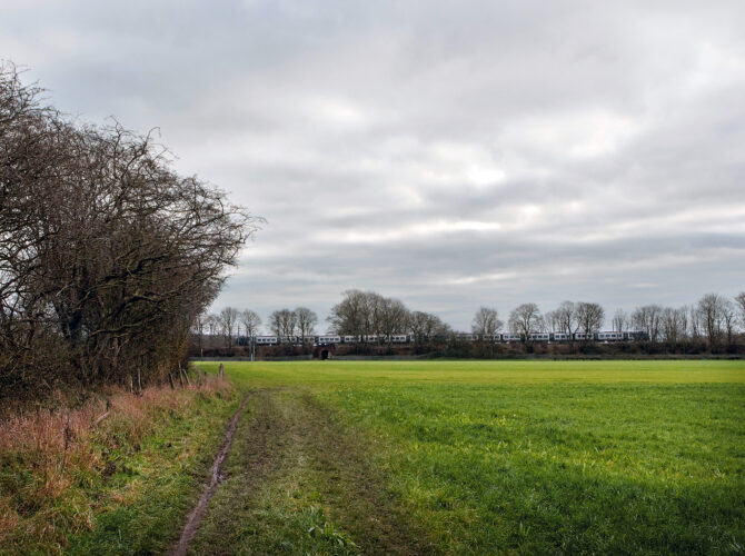 Passenger train crossing a low brick bridge across open fields on Chat Moss