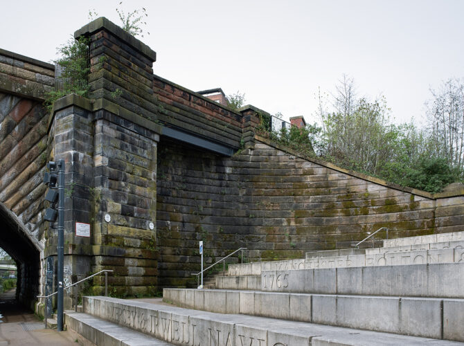 A surviving curved stone retaining wall on the Salford side of the River Irwell, showing where the original railway bridge once connected to Eccles Bridge before its removal