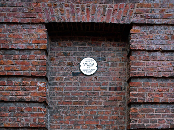 Close-up of a recessed brick panel containing a commemorative plaque identifying the location of the Grade II listed 1837 Arrivals Station.