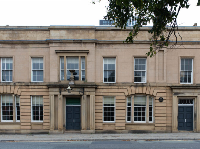 Close view of the adjoining station building with ashlar detailing, arched ground-floor windows, and central entrance.