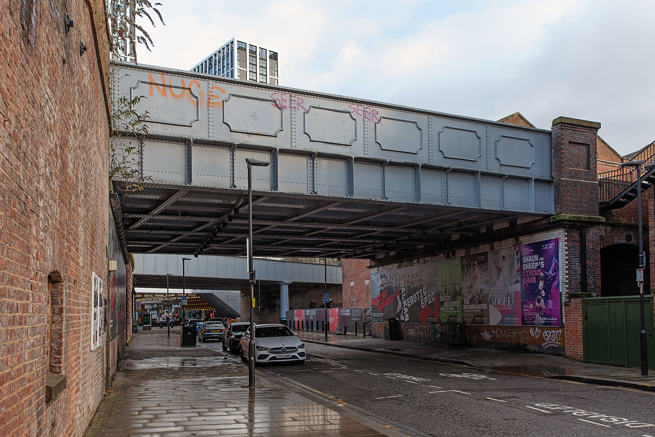 Wider view of the bridge spanning the road, with nearby buildings, signage, and traffic passing underneath.