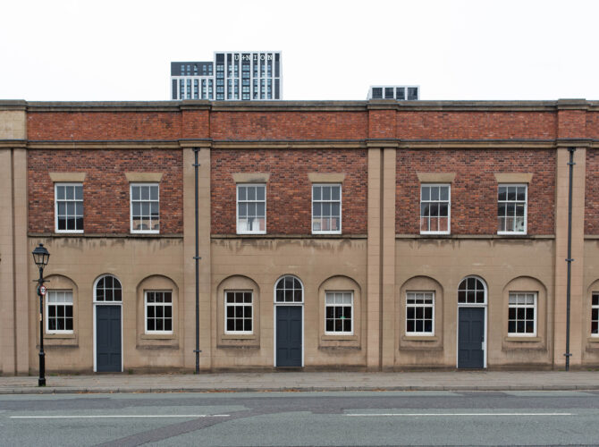 View along the extended range of brick and stone station buildings, showing regularly spaced doors and windows.