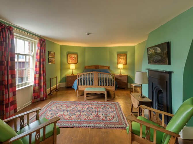 Period-style bedroom with painted walls, fireplace, and traditional furnishings reflecting domestic use of the house.