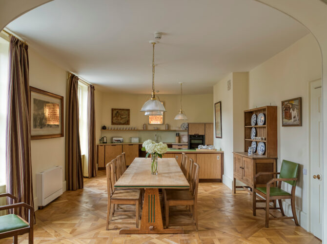 Spacious dining area with wooden table, chairs, and open-plan kitchen space beyond, set within a historic interior.