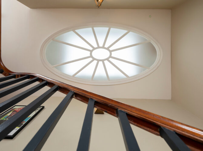 View upward along a staircase to an oval skylight, highlighting architectural detailing within the house.
